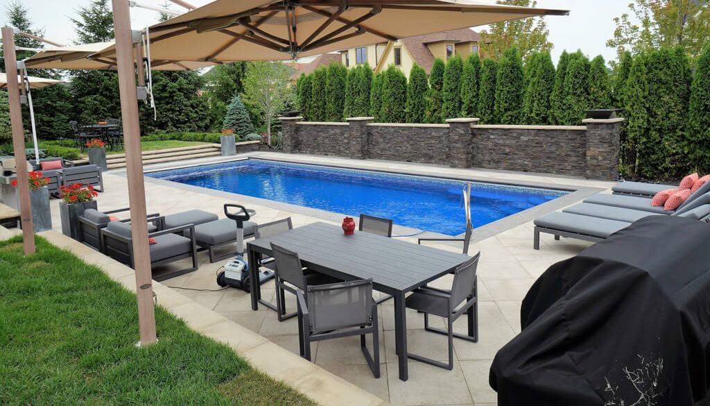 A backyard with a swimming pool, lounge chairs, a dining table, and greenery surrounding the area.