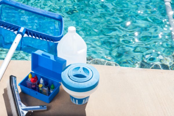 Swimming pool maintenance supplies including water testing chemicals, chlorine, and cleaning equipment beside a pool.