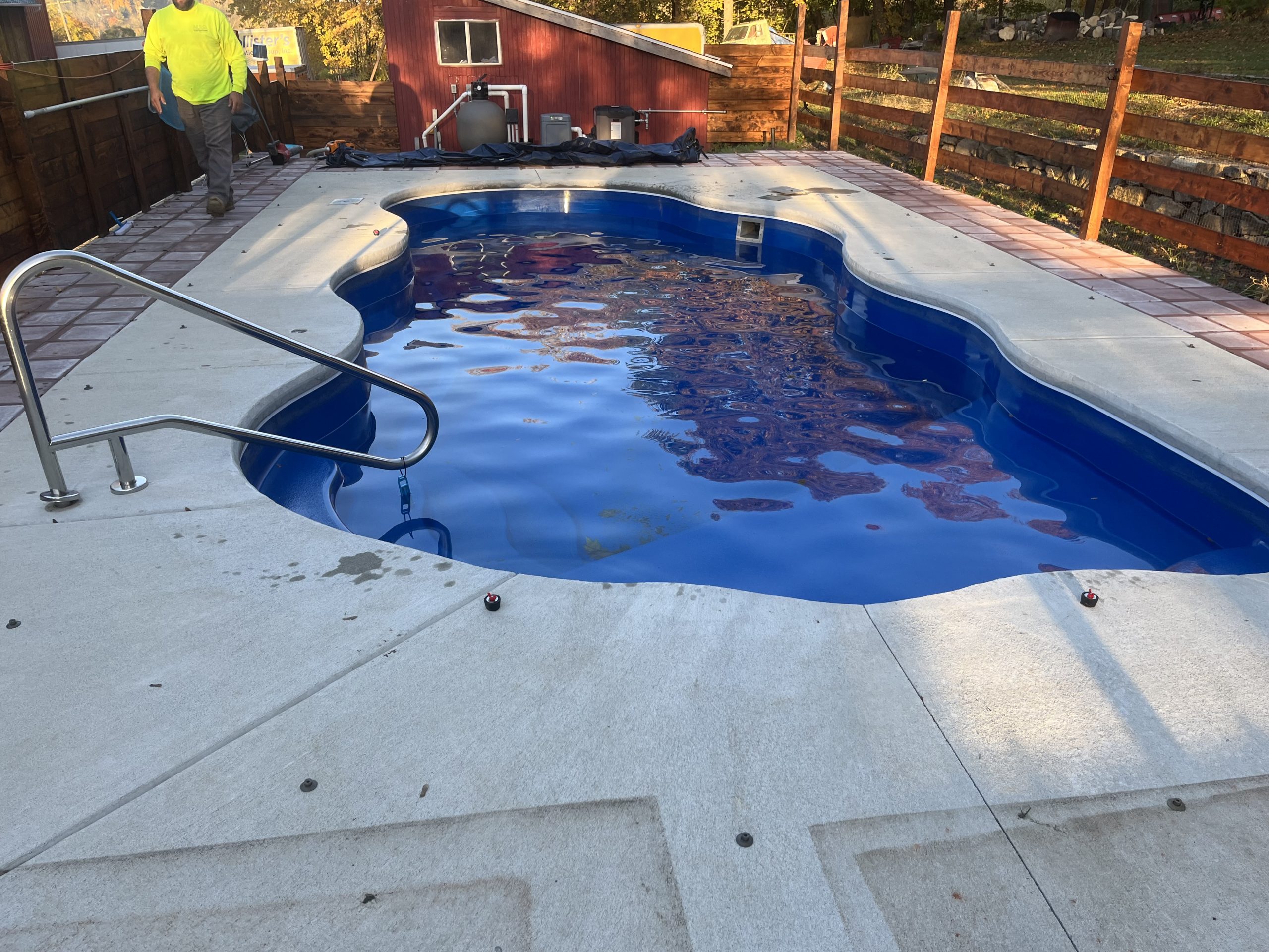 Freeform fiberglass swimming pool with freshly cleaned water and surrounding concrete deck after pool service.