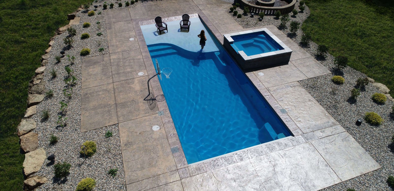 Aerial view of a swimming pool with two chairs, a hot tub, and landscaped surroundings.