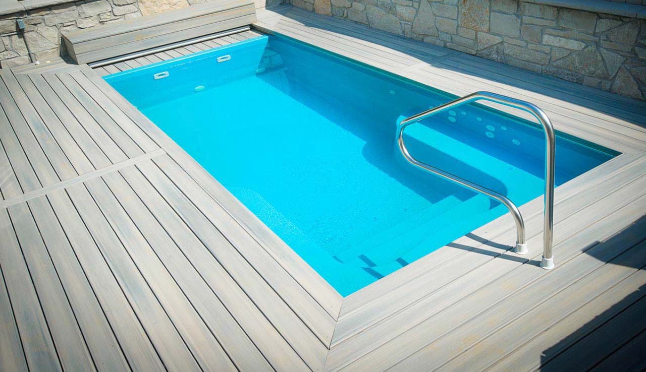 High-angle view of a Sea Turtle rectangular fiberglass pool featuring bright cyan water, built-in entry steps, stainless steel handrail, and light grey composite wood decking.