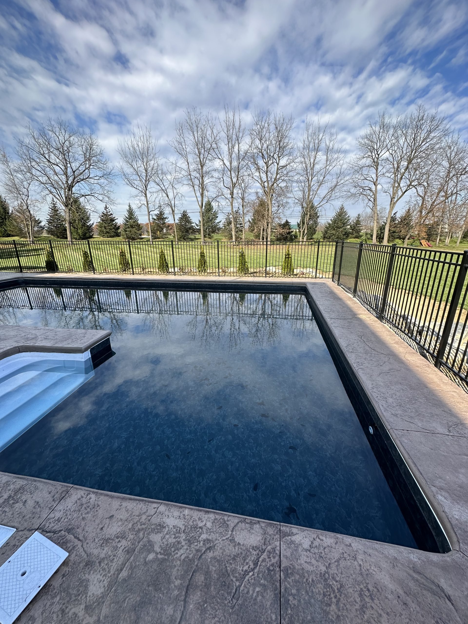 Rectangular fiberglass swimming pool prepared for seasonal opening with clean water and a secure backyard fence.