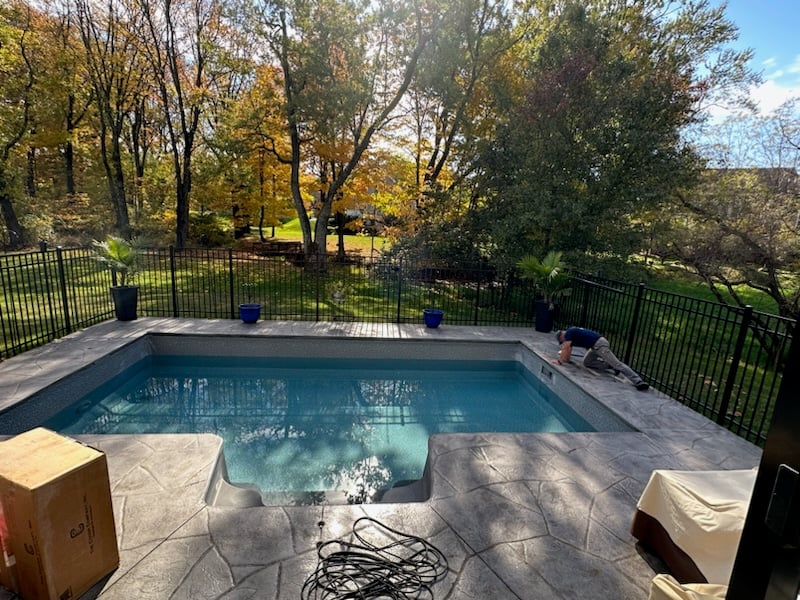 Backyard in-ground swimming pool professionally opened with balanced water and a clean surrounding patio.
