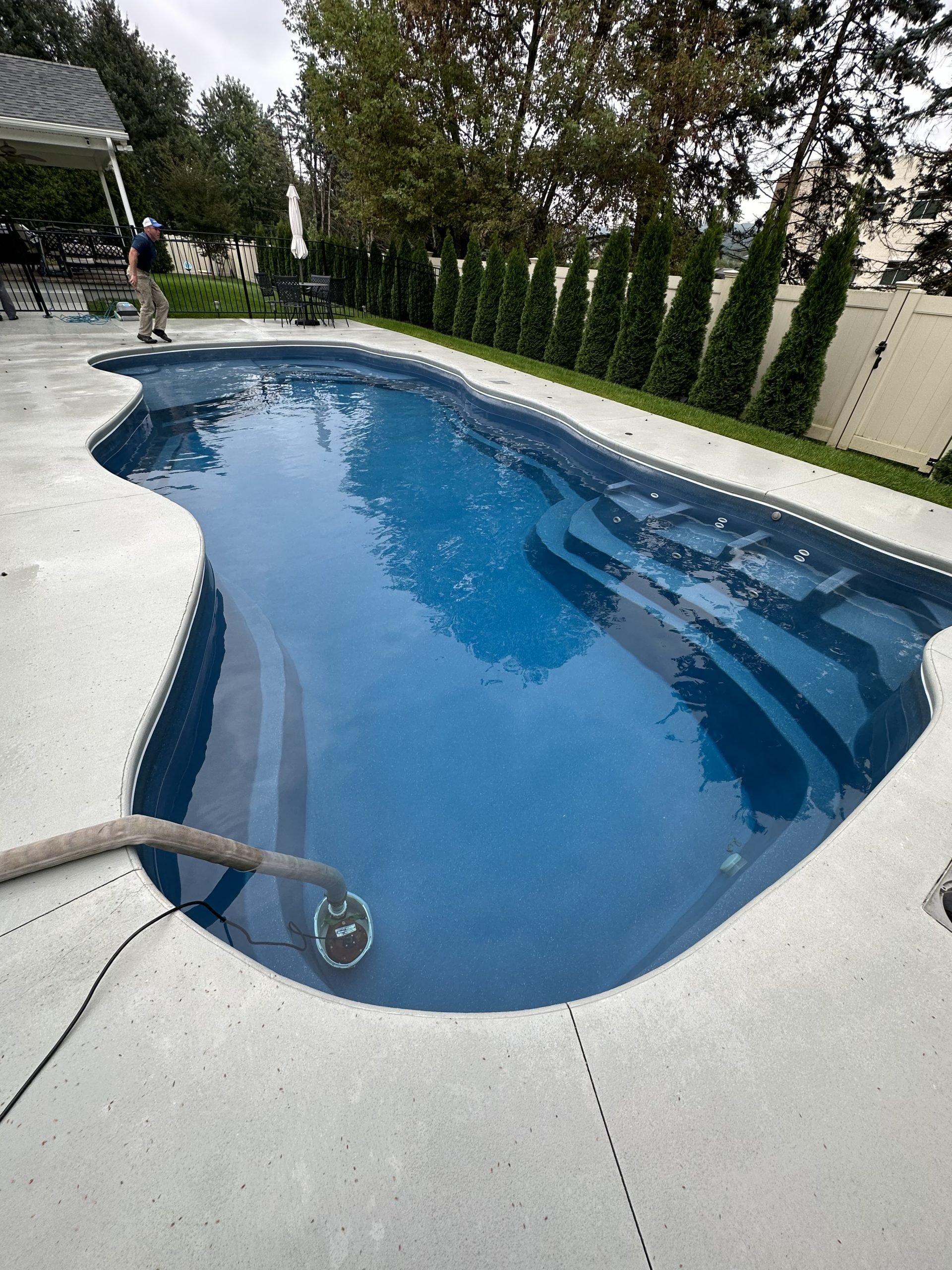 Freeform fiberglass swimming pool with entry steps and clear blue water after professional pool maintenance.