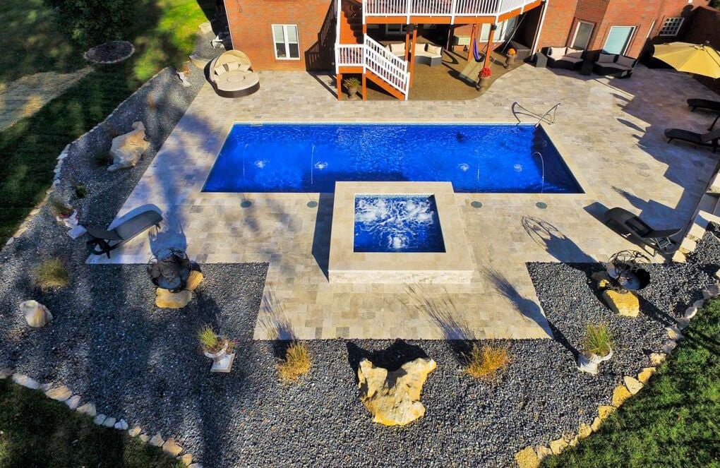 Aerial view of a backyard with a blue swimming pool, spa, patio, and landscaped stones.